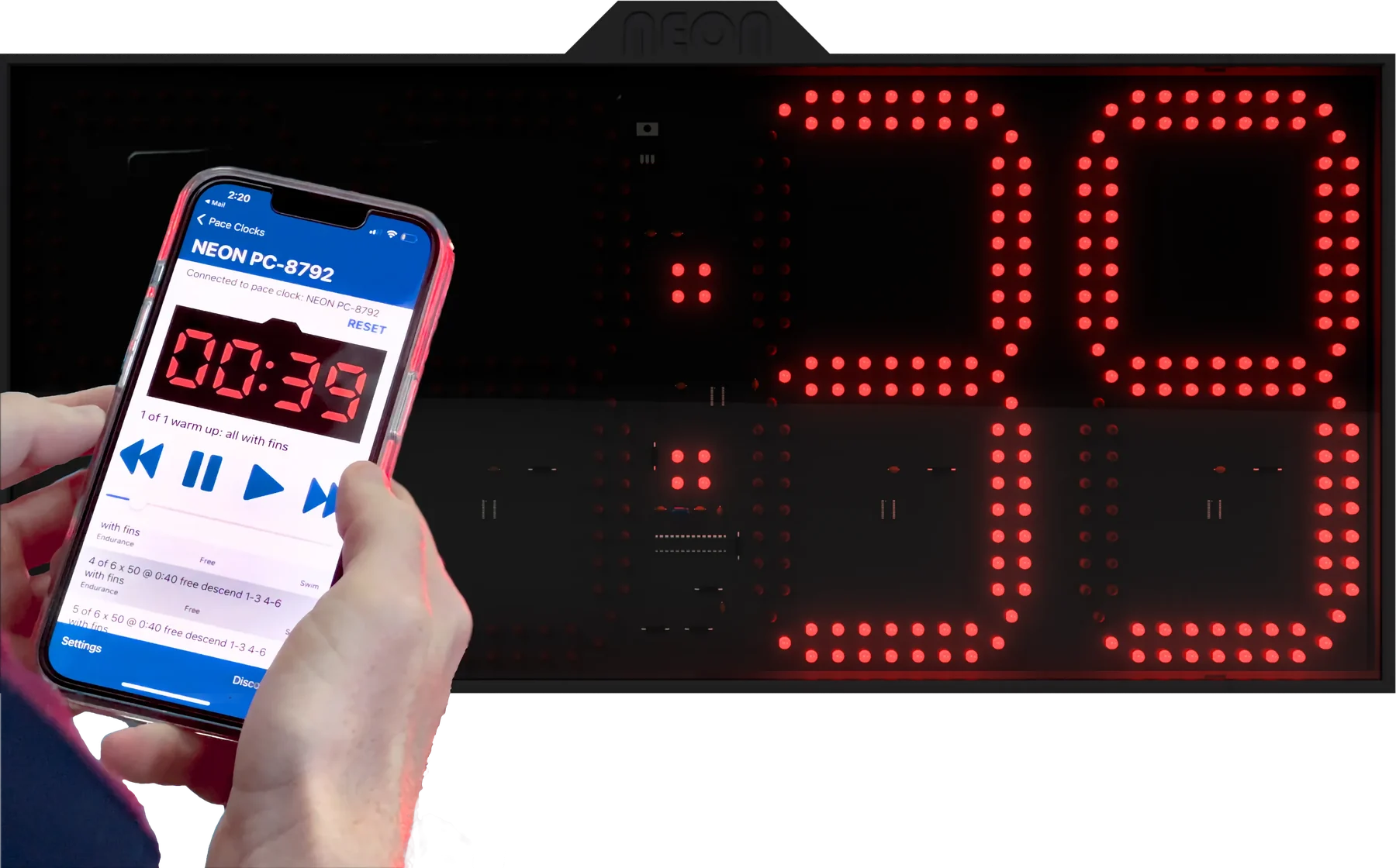A hand holding a phone running the Neon Swim app next to a Neon pace clock. Both read 39 seconds into the interval.