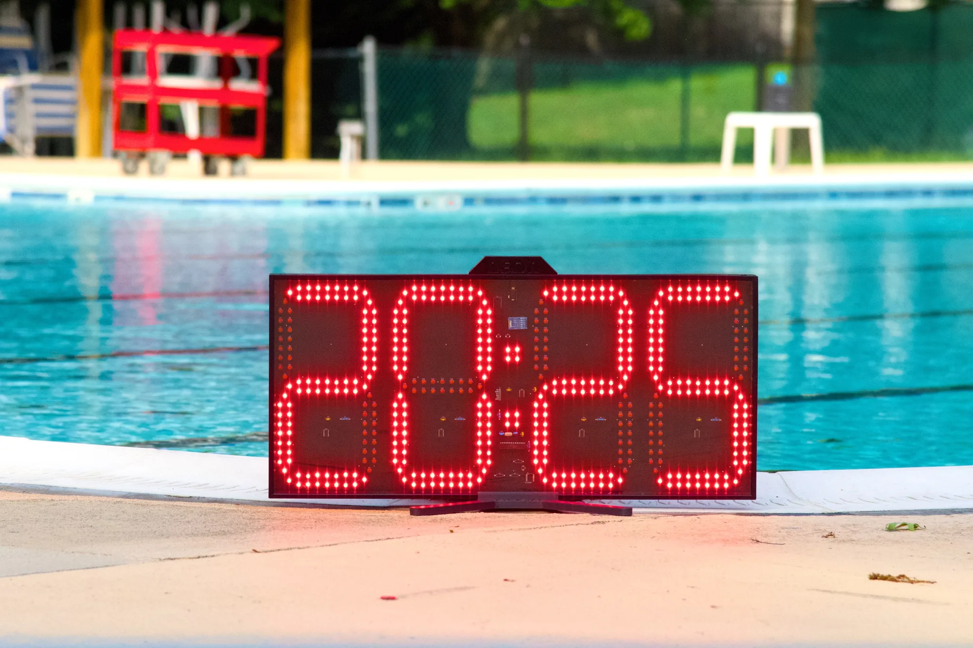 A Neon pace clock reading 20:26 on the deck of an outdoor pool